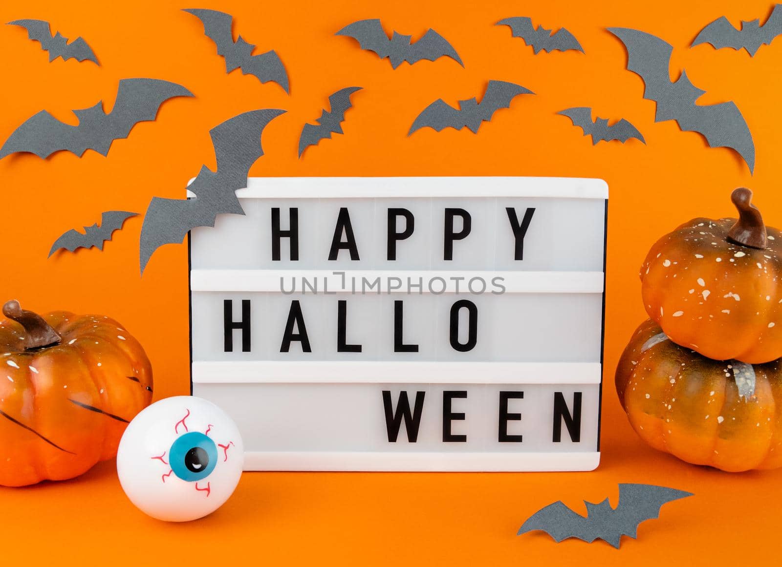 Light box with Happy Halloween phrase with pumpkins, bats and eyeball decoration on orange background.