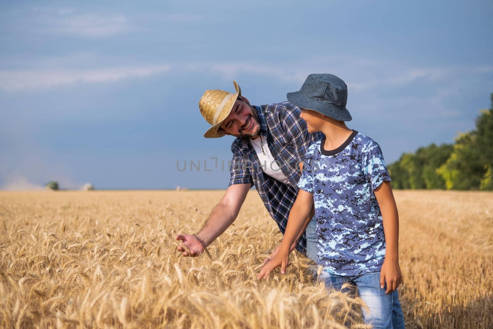 Happy father and son are standing in their grown wheat field before harvest.