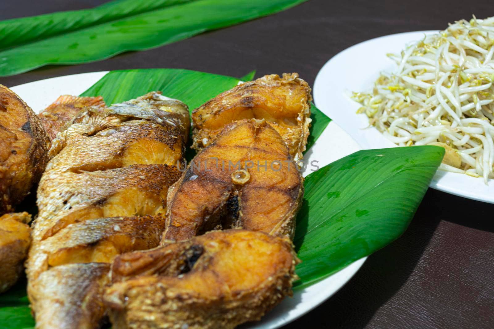 Fried fish on plate with green leaf on dark background