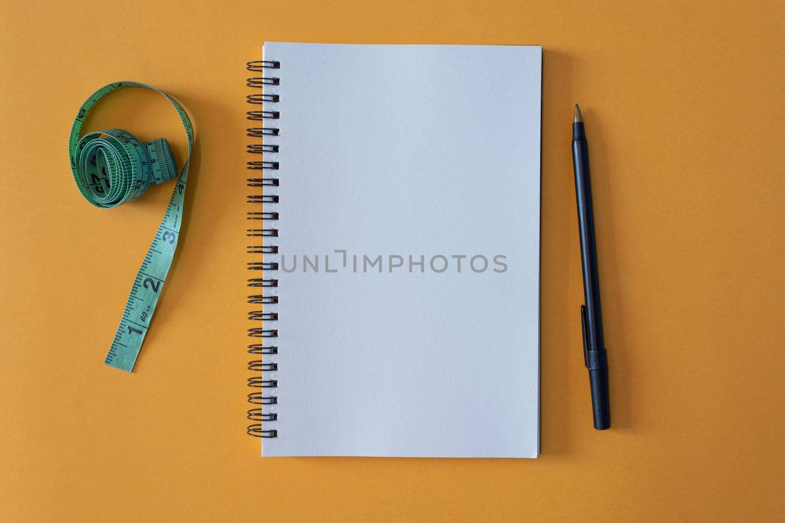 Notepad with pen and measurement tap on yellow background. Space for text