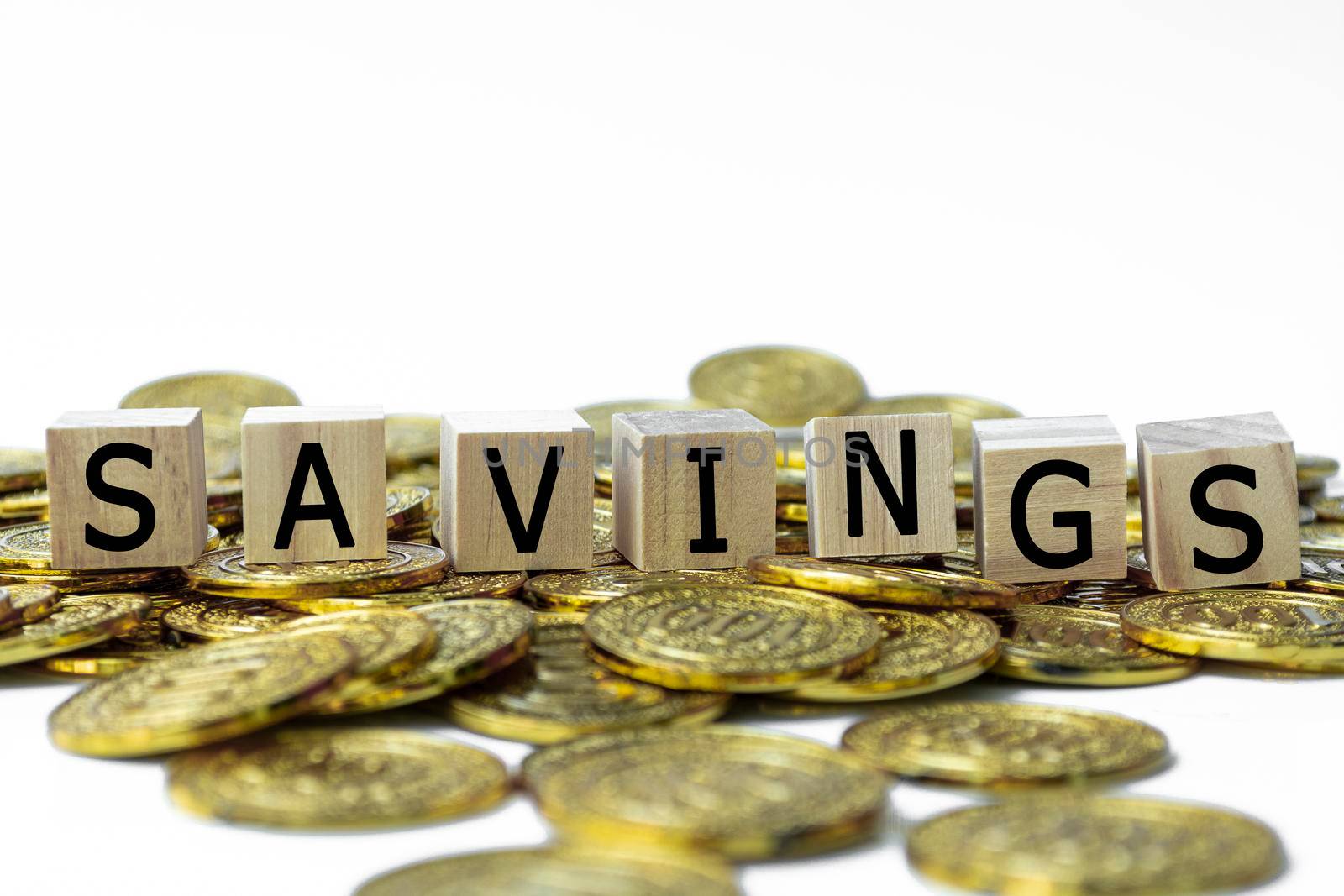 Savings text on wood block with blurred background of a pile of gold coins