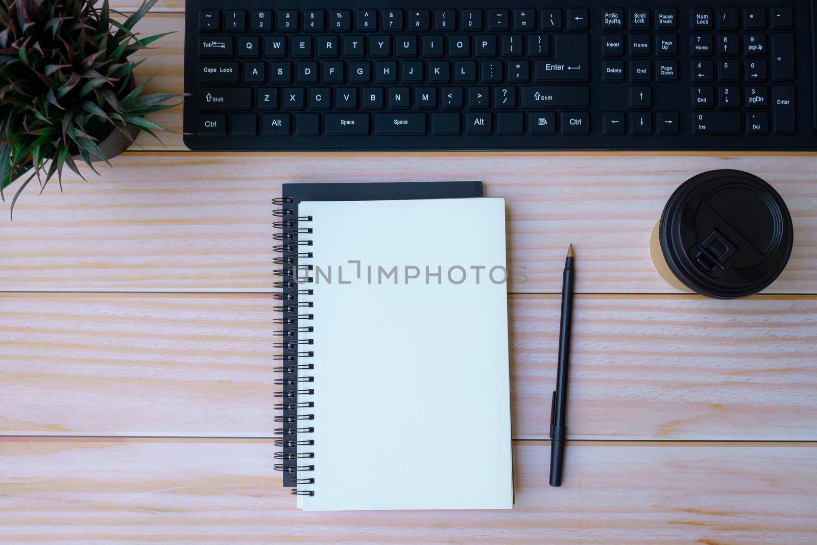 Home office space with keyboard, note books, pen, coffee cup and potted plant on wooden table. Space for text. Flat lay, top view