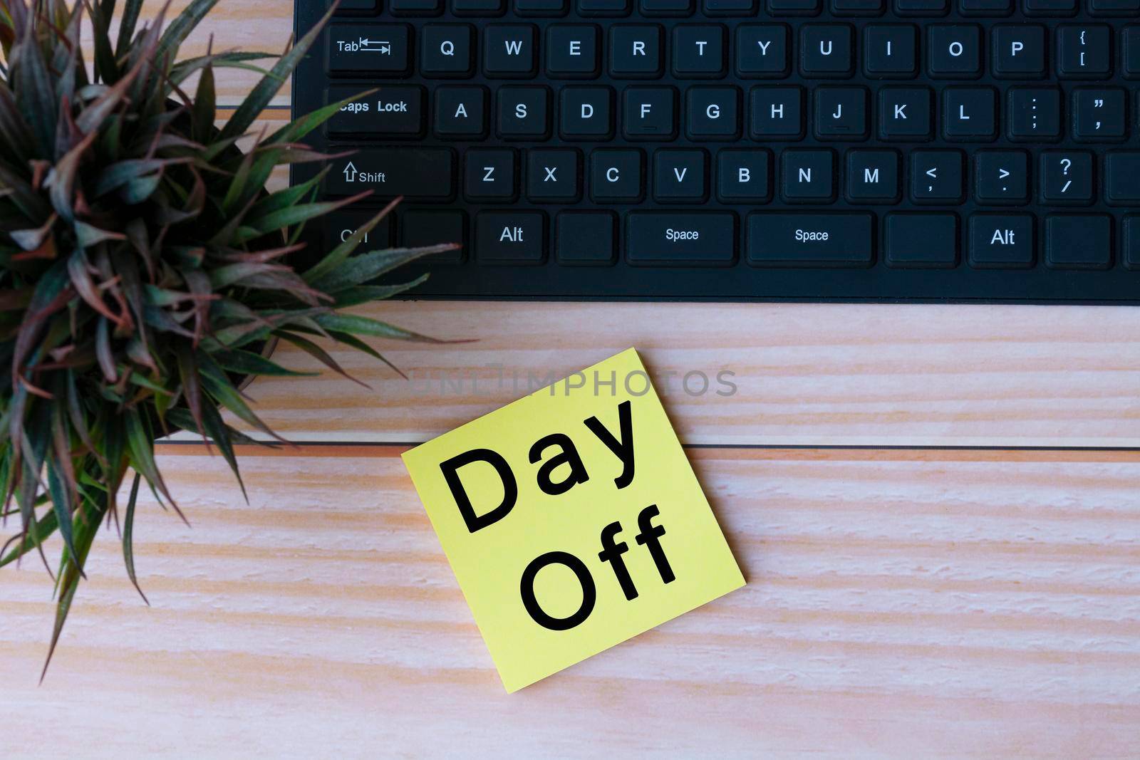 Text on yellow note with keyboard and potted plant on wooden table. Day off