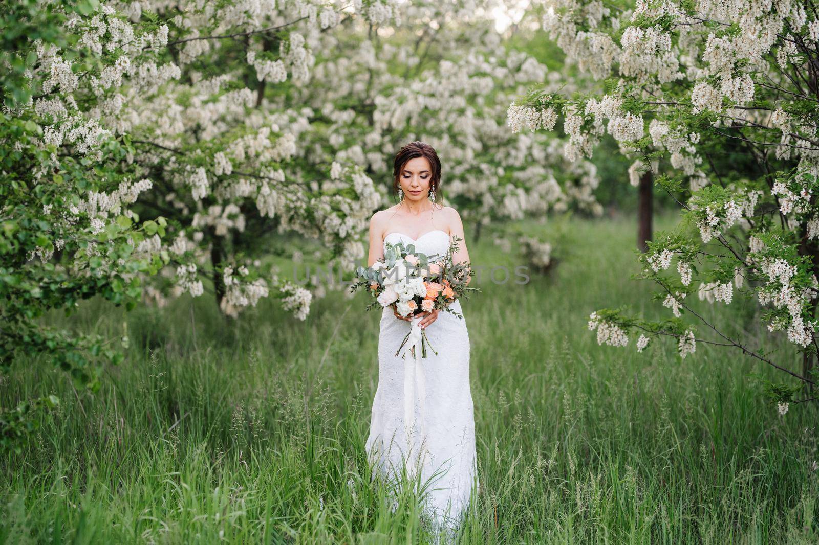 bride in a white dress with a large spring bouquet in a green forest