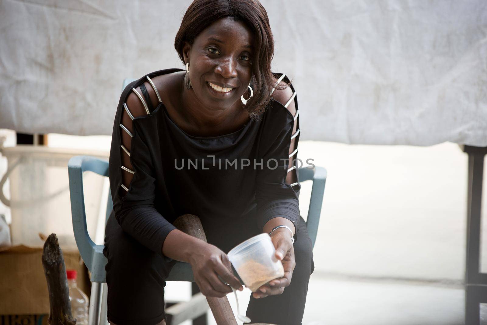 Smiling saleswoman sitting at the market behind her display and pounding the dried spices