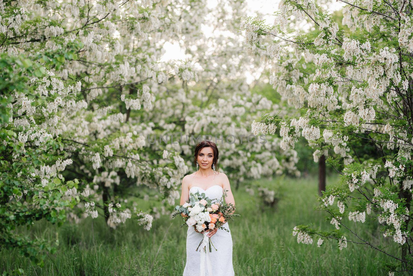 bride in a white dress with a large spring bouquet in a green forest