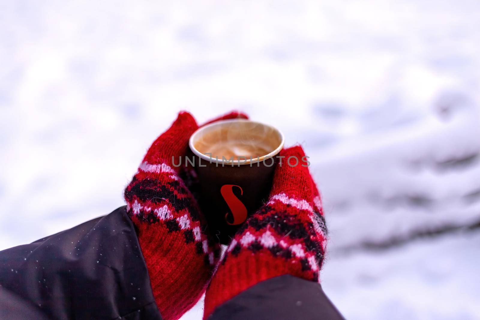 Women's hands in a red mittens hold a paper cup of coffee by clusterx