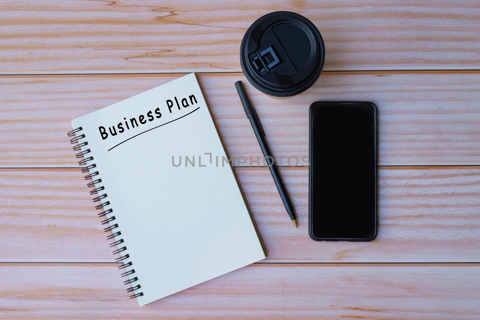 Business plant text on notepad with pen, coffee and smartphone on wooden table. Space for text. Flat lay, top view