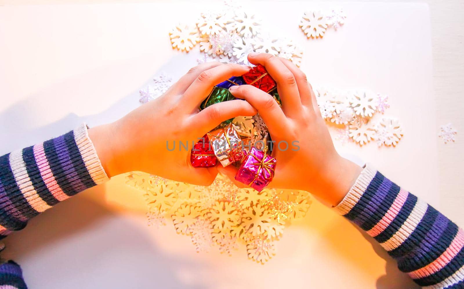 Small paper snowflakes and bright colorful gift boxes in child's hands. Cristmas and New Year gift decoration process.