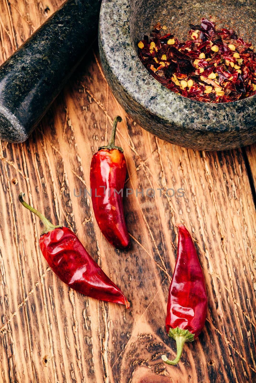 Dried red chili peppers on wooden surface with mortar and pestle by Seva_blsv