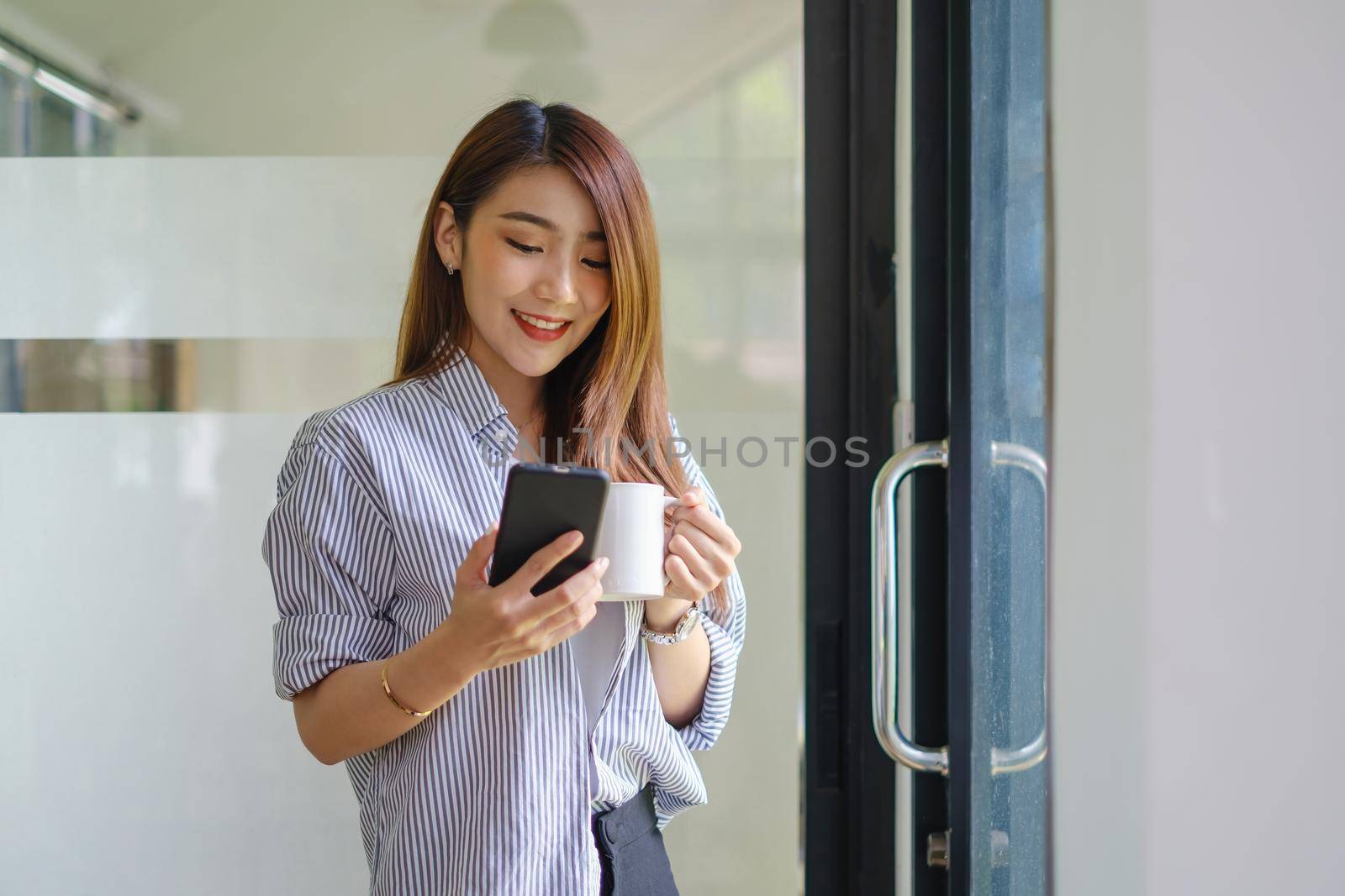 Young beautiful woman holding coffee cup and feeling fresh while sitting at her working place at monday morning