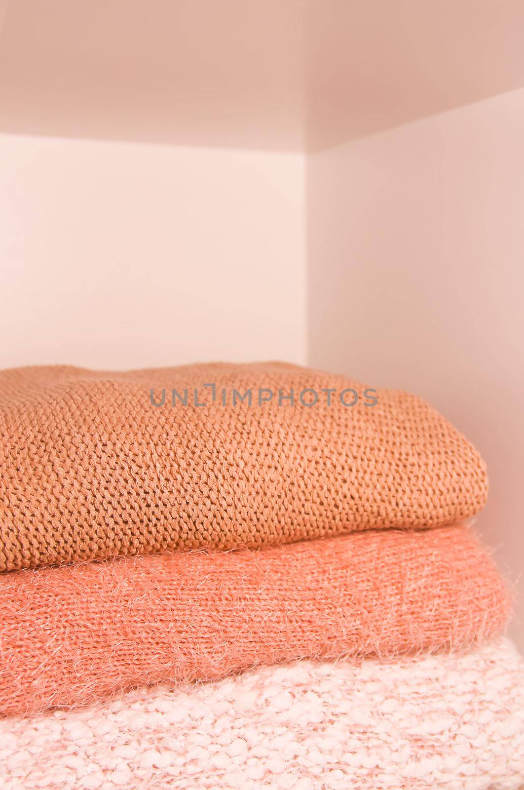 Pile of warm autumn and winter knitted sweaters on a home wardrobe shelf. Modern fashion clothes in shades of living coral.