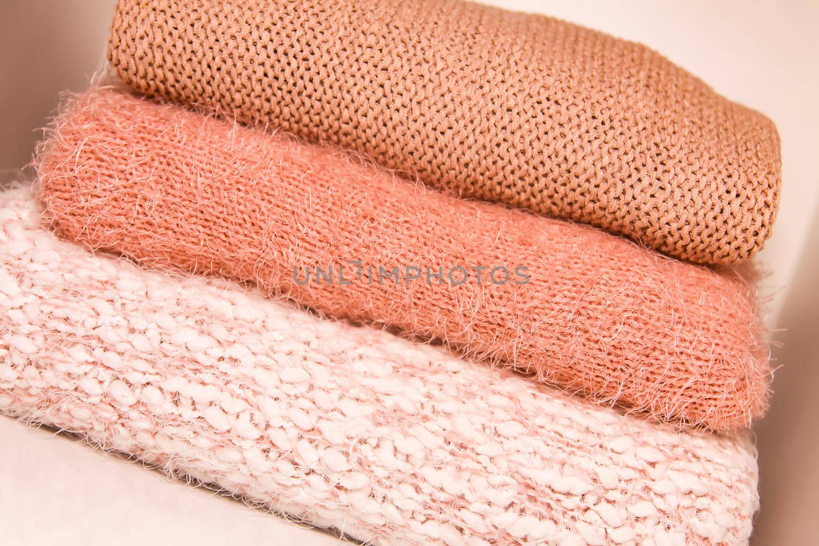 Pile of warm autumn and winter knitted sweaters on a home wardrobe shelf. Modern fashion clothes in shades of living coral by nightlyviolet