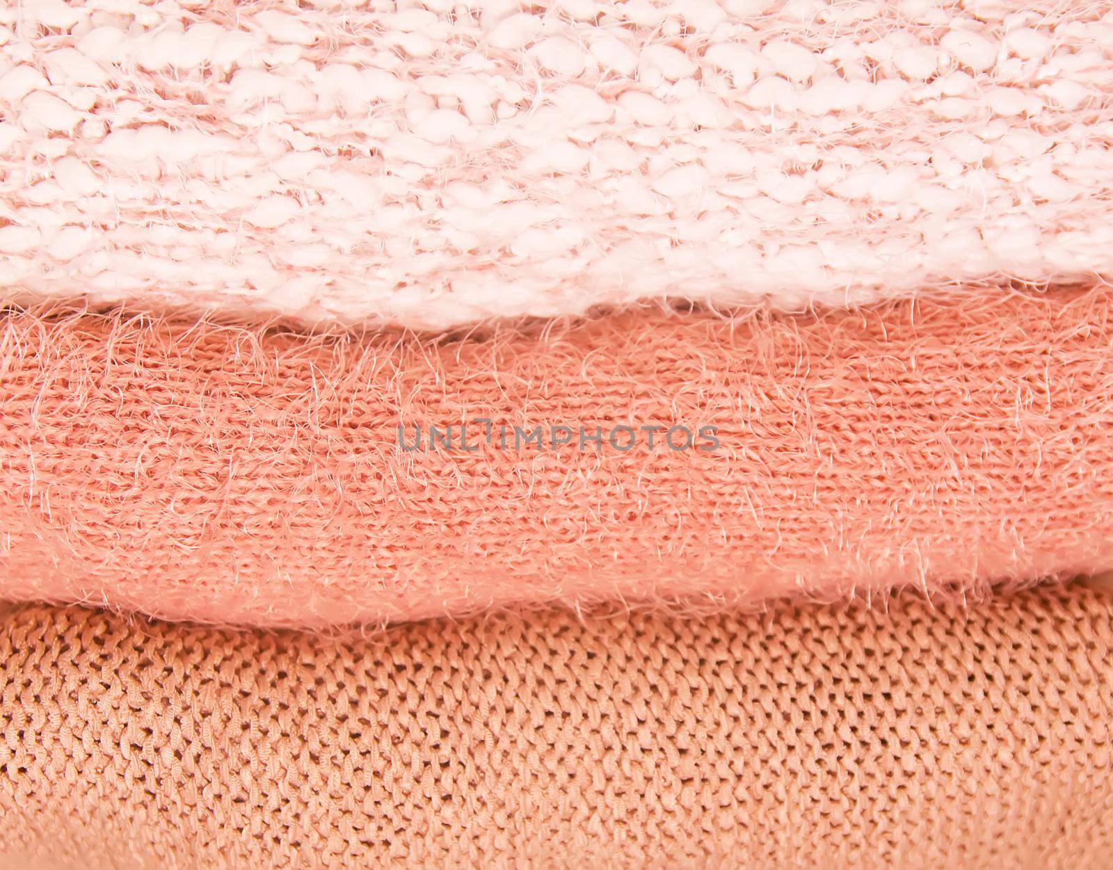 Pile of warm autumn and winter knitted sweaters on a home wardrobe shelf. Clothes in color of living coral. by nightlyviolet