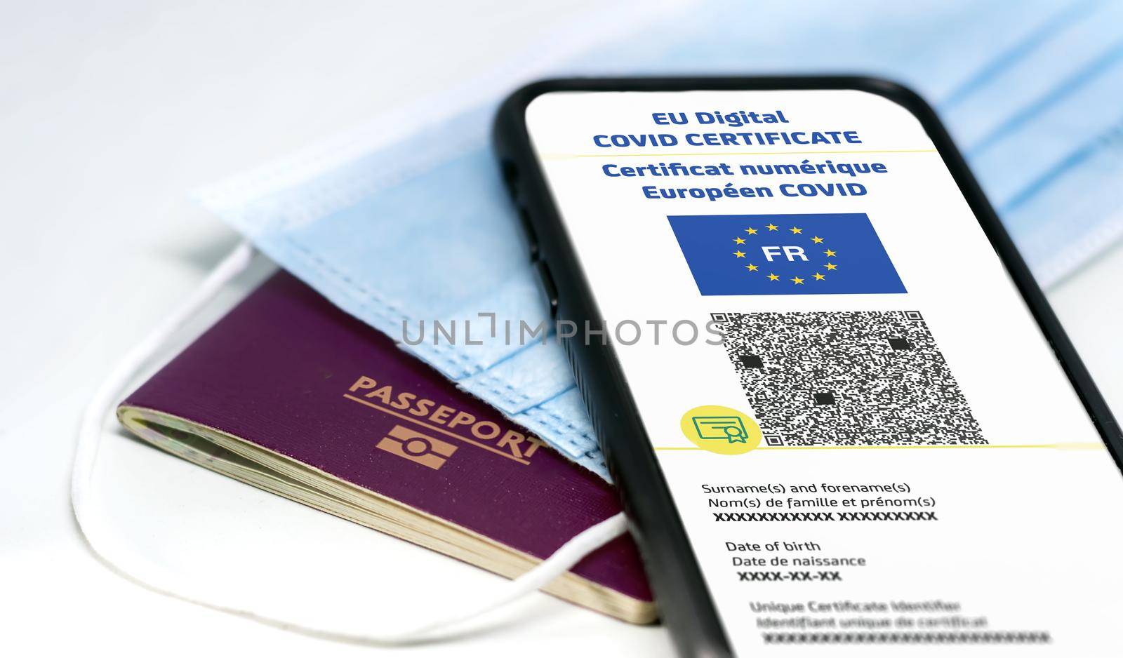 French EU Digital COVID Certificate with the QR code on the screen of a mobile phone over a surgical mask and a french passport by rarrarorro