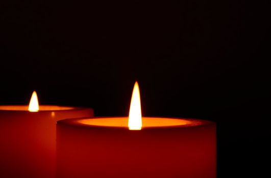 Two big burning candles, close up, on a black background.