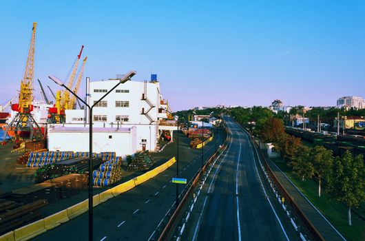 The road from seaport to the city, port cranes railway cars, city buildings on a background.