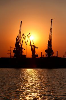 Silhouettes of port cranes against a solar disk at sunset. The Odessa seaport, Coasting harbour. Ukraine.