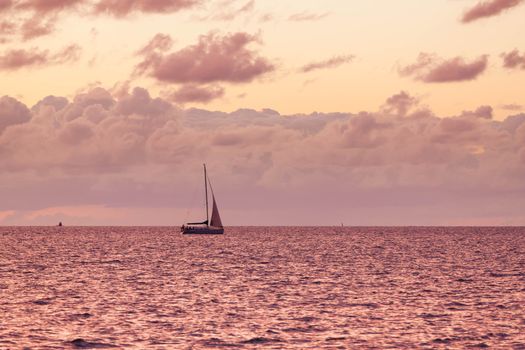 A solitary sailboat in the open sea at the sunse