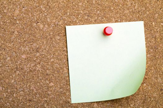 A sticky note with a curled up corner on a corkboard