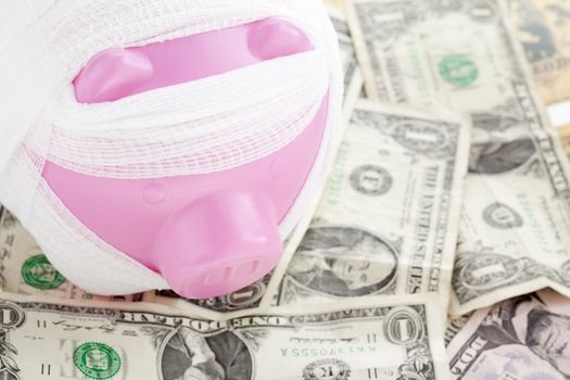Closeup shot of bandaged pink piggy bank on American dollars.