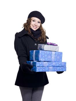 Portrait of a smiling young woman in winter clothing holding a stack of gift boxes over white background, Model: Brittany Beaudoin