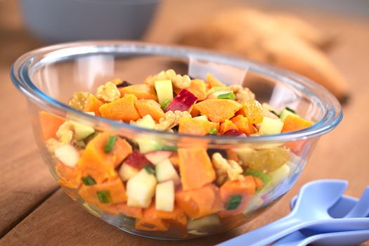 Glass bowl of fresh salad made of cooked sweet potatoes, fresh apples, nuts, raisins and shallots (Selective Focus, Focus one third into the salad)