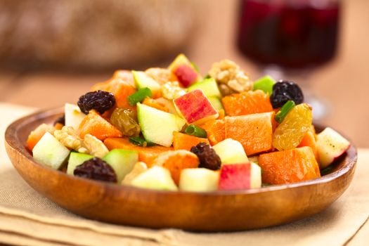 Fresh salad made of cooked sweet potatoes, fresh apples, nuts, raisins and shallots on wooden plate with mulled wine in the back (Selective Focus, Focus one third into the salad)