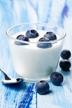 Yogurt in glass with blackberry on blue wooden table