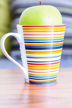 Green apple in colorful cup on wooden table