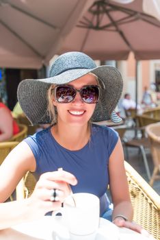 Beautiful young woman in hat and sunglasses at street cafe