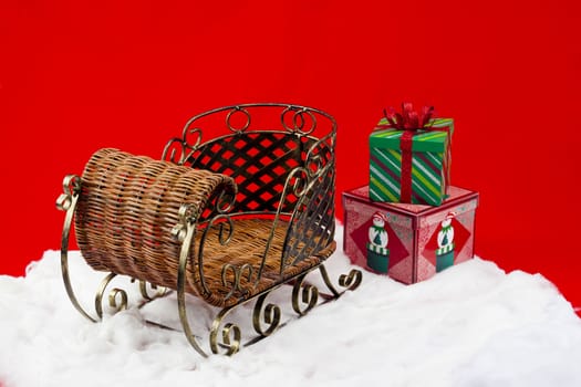 Shot of a wicker sleigh on faux snow with presents laying in the snow outside of of it.