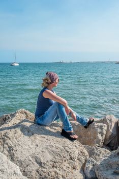 Young woman sitting on rock and watching the mediterranean sea
