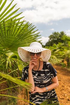 Young woman in hat and sun glasses near palm