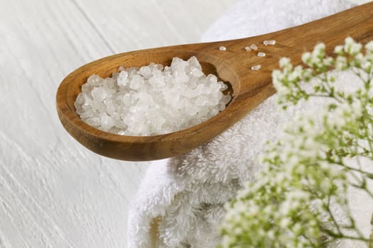 A spoon of spa salt and a white towel on a wooden background 