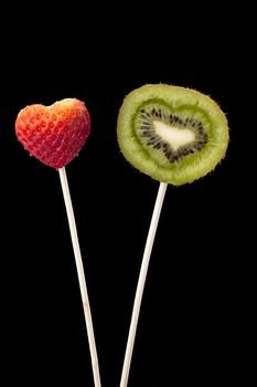 Isolated image of a heart shape strawberry and sliced kiwi fruit in stick against a black background