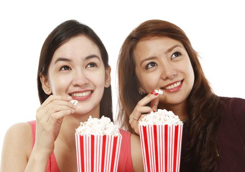 Two young women eating popcorn while watching a movie (on white background)