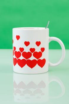 White cup with red hearts on green background