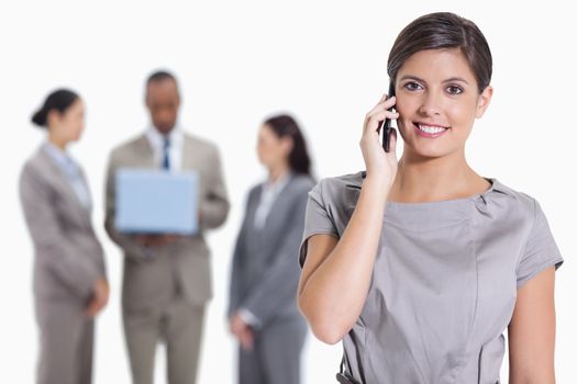 Close-up of a woman smiling on the phone and co-workers with a laptop in the background