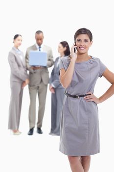 Businesswoman on the phone with a hand on her hip and crossing her legs, with co-workers in the background with a laptop