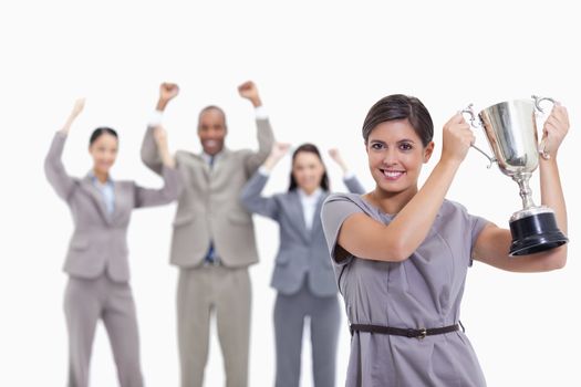 Close-up of a woman smiling and holding up a cup with co-workers raising their arms in the background