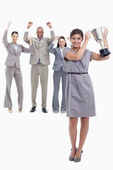 Picture centered on woman smiling and holding up a cup with co-workers raising their arms in the background 