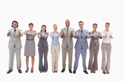 Smiling business team side by side with their thumbs up against white background