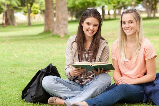 Female teenagers sitting with a textbook in a park while looking at camera
