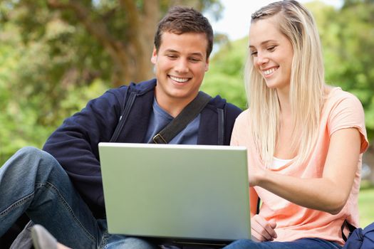 Young people sitting while using a laptop in a park