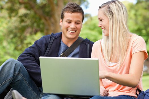 Laughing young people sitting while using a laptop in a park