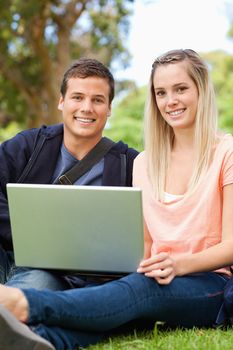 Portrait of young people laughing while sitting with a laptop in a park