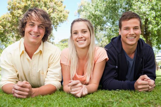 Portrait of three smiling students in a park lying on their tummy