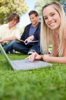 Close-up of a girl using a laptop while lying in a park with friends in background