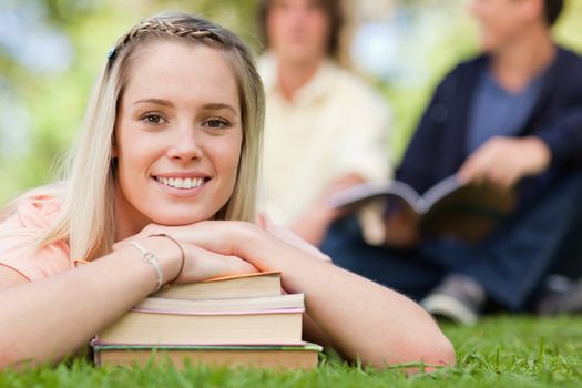 Portrait of a girl lying head on her books in a park with friends in background